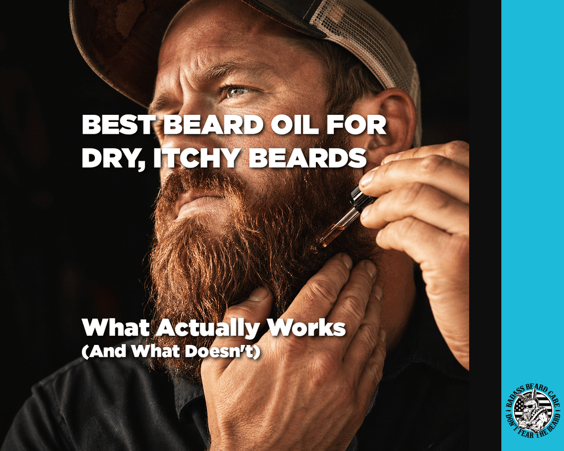 Close-up portrait photograph of a rugged man in his 30s with a thick, full dark red beard, applying Badass beard oil from an amber glass dropper bottle. His fingers work the oil into his beard near the jawline.